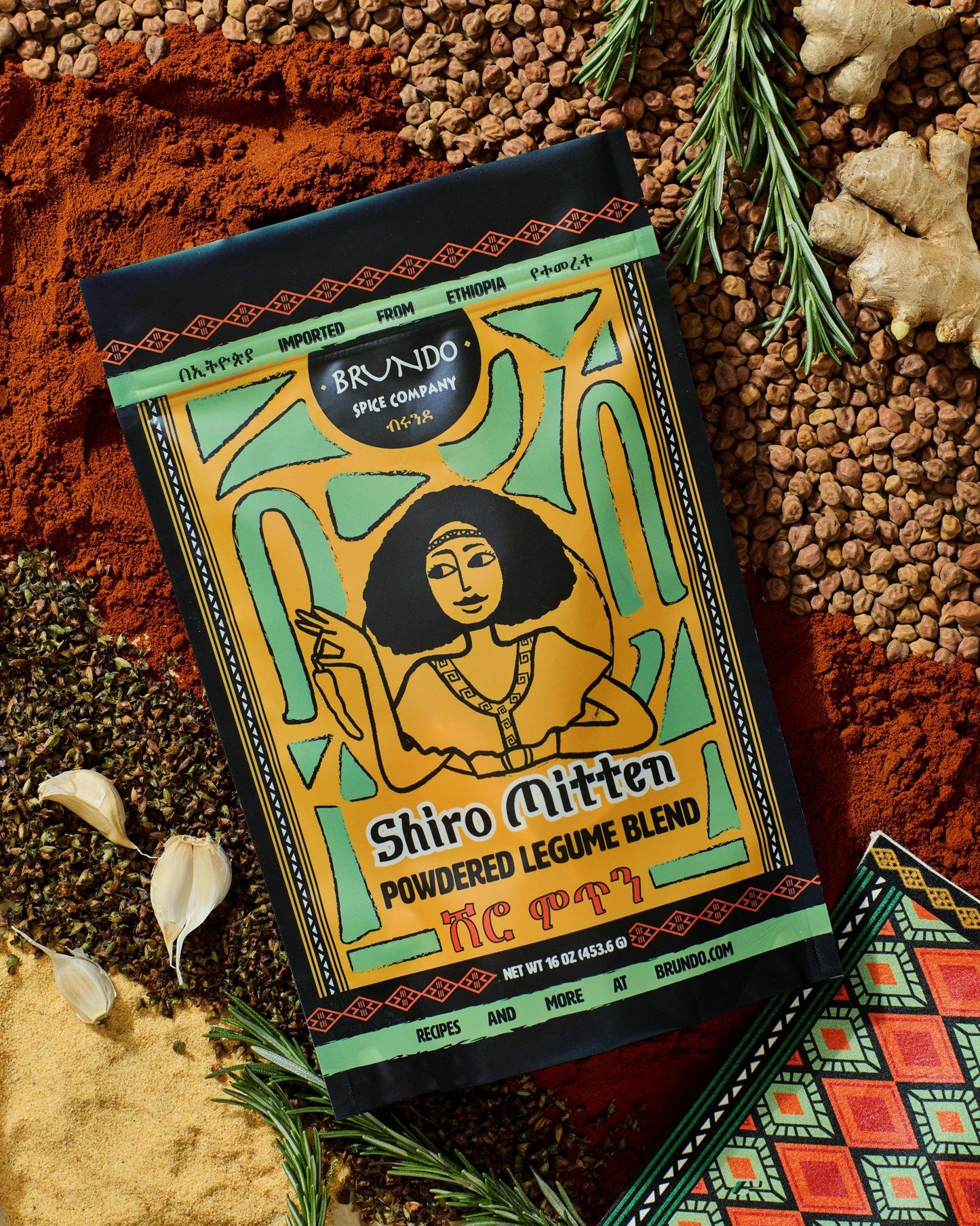 Brundo Spice Company Shiro Mitten Powdered Legume Blend pouch displayed with garlic, rosemary, chickpeas, ginger, and a traditional napkin.
