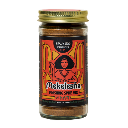 Brundo Spice Company Mekelesha Finishing Spice Mix jar surrounded by green cardamom, cloves, cinnamon bark, black pepper, and fenugreek.