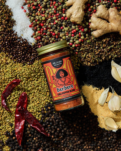 Brundo Spice Company Berbere Chili Pepper Blend pouch surrounded by garlic, dried chilies, ginger, and a variety of whole spices.