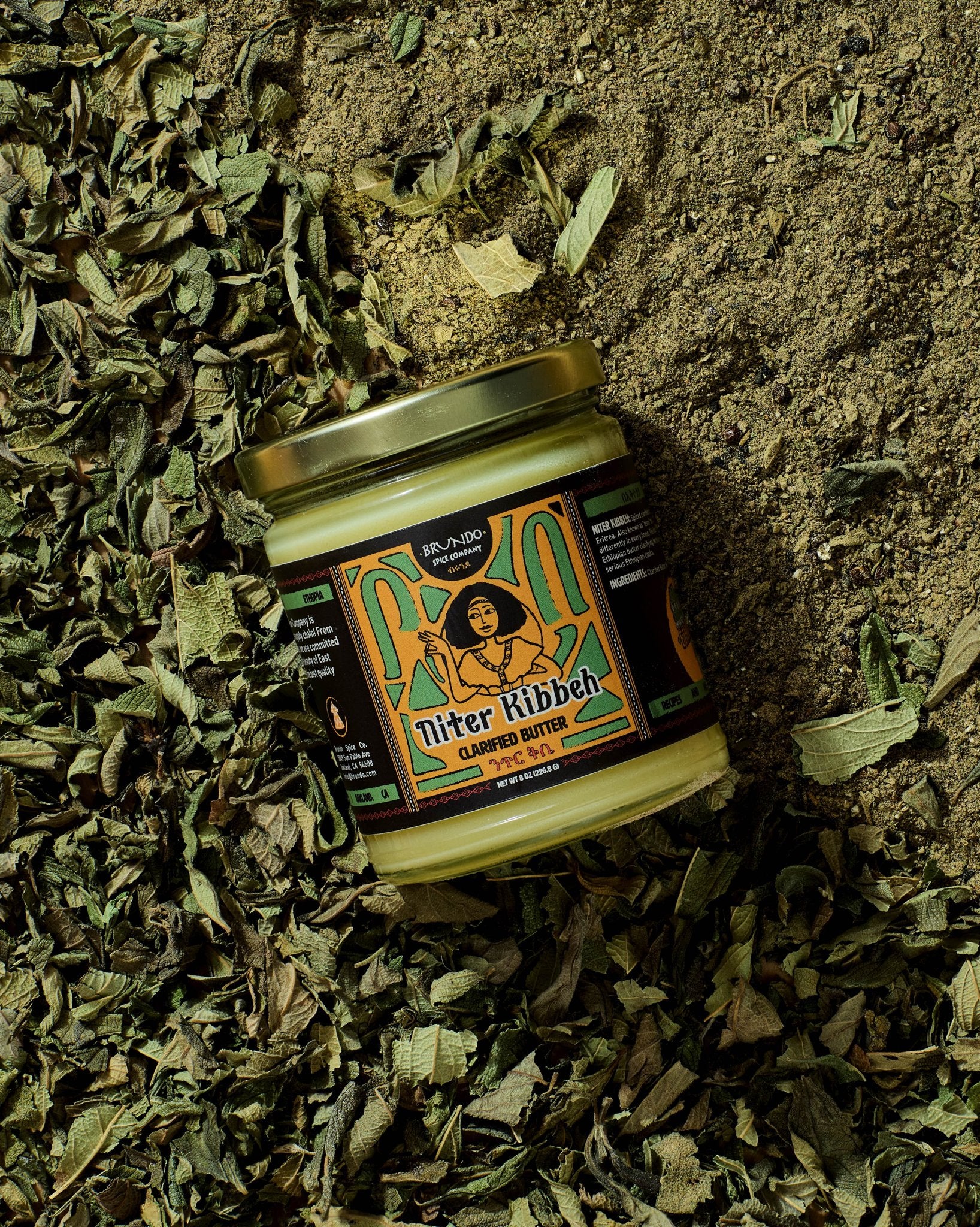 Brundo Spice Company Niter Kibbeh Ethiopian clarified butter jar placed on a bed of dried koseret and besobela herbs.