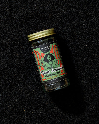 Brundo Spice Company Tikur Azmud Wild Nigella Seed jar placed on a dark bed of whole black nigella seeds.